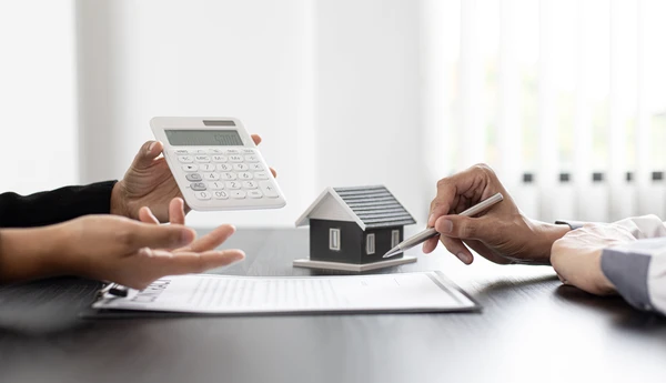 Une main tient un stéthoscope médical au-dessus d'une maquette de maison résidentielle posée sur un bureau avec ordinateur portable en arrière-plan, symbolisant l'inspection ou le diagnostic immobilier