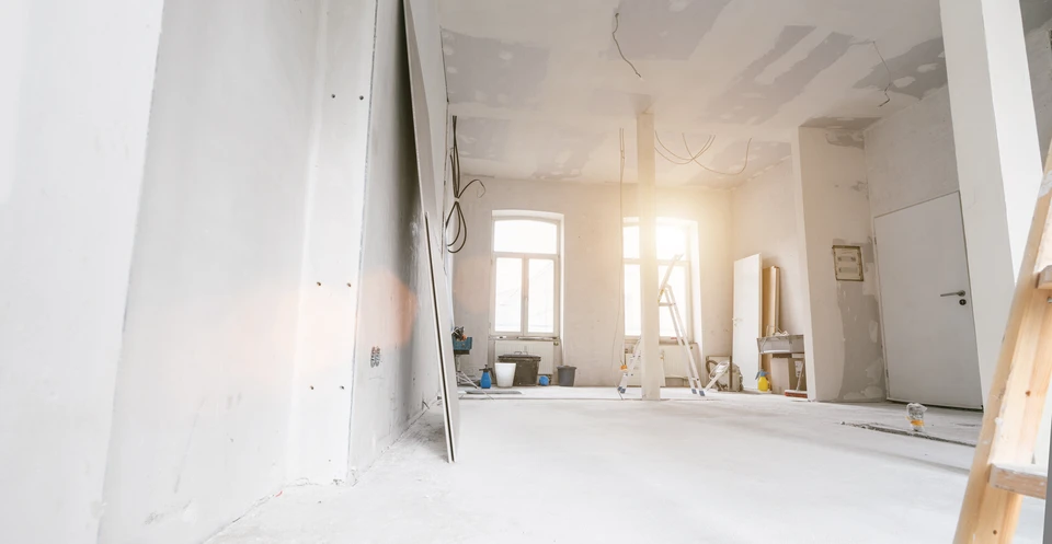 Chantier de construction extérieur avec homme en tenue de travail, casque de sécurité jaune, bras croisés devant bâtiments en construction