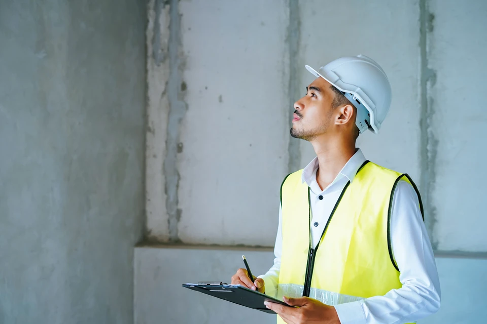 Inspecteur en bâtiment examine un chantier de construction intérieur, portant casque de sécurité blanc et gilet haute visibilité jaune réfléchissant