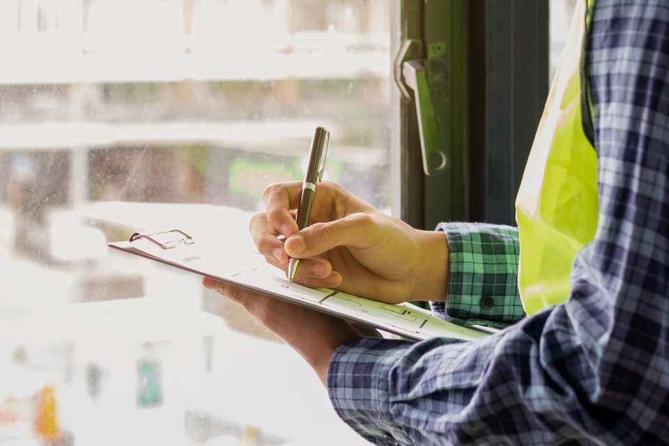Professionnel en uniforme bleu devant pavillon résidentiel, tenant clipboard et stylo