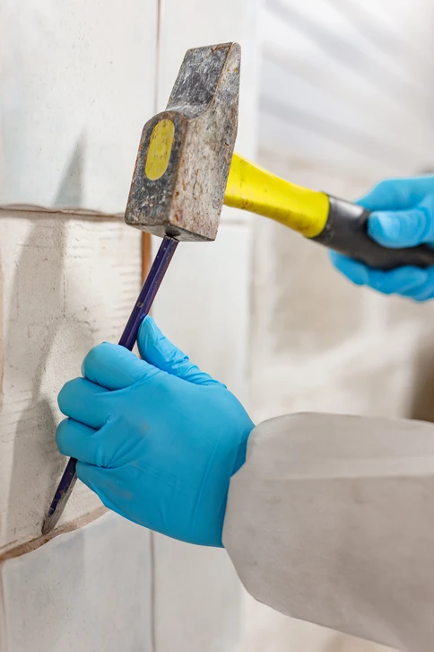 Diagnostiqueur en combinaison blanche de protection et masque FFP3, utilisant un perceuse ou un outil de prélèvement pour collecter un échantillon de flocage au plafond dans un intérieur résidentiel. L'accent sur le geste technique précis du diagnostic amiante, en environnement réel de bâtiment ancien.